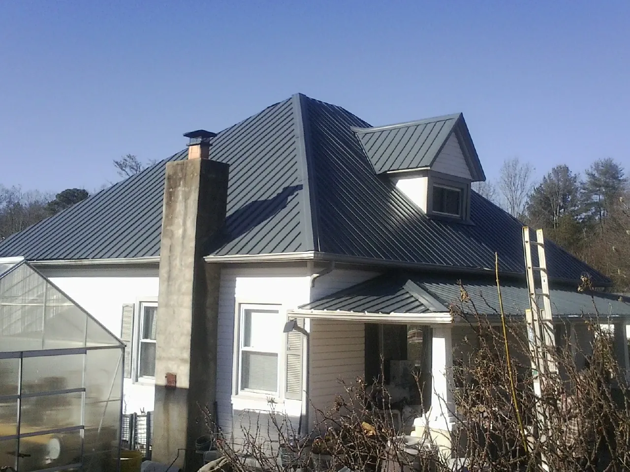 Dark blue standing seam metal roof on a white farmhouse with dormer — Slate & Tile Roof Repair by Roofing Brothers in North Norwich
