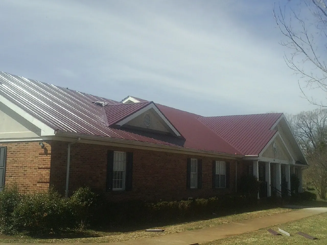Red metal roof with gabled entries on a long brick building, from a Hail Damage Roof Repair job in North Norwich