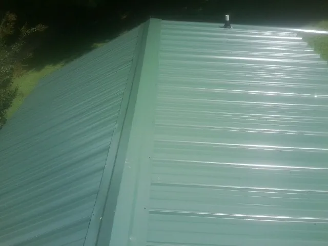 New green metal panels meeting at the ridge of a roof — Flat Roof Repair work by our crew in North Norwich