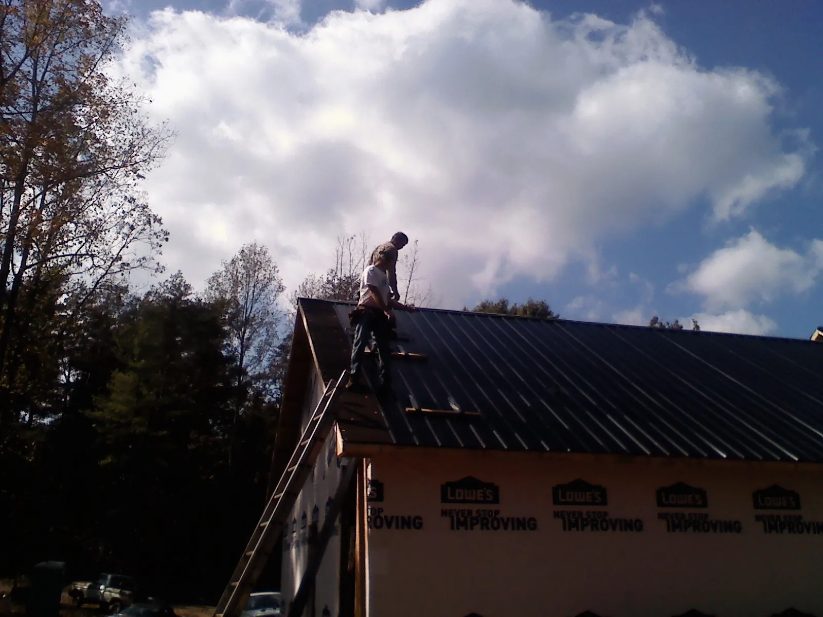 Roofer fastening dark metal panels high against a cloudy sky in North Norwich