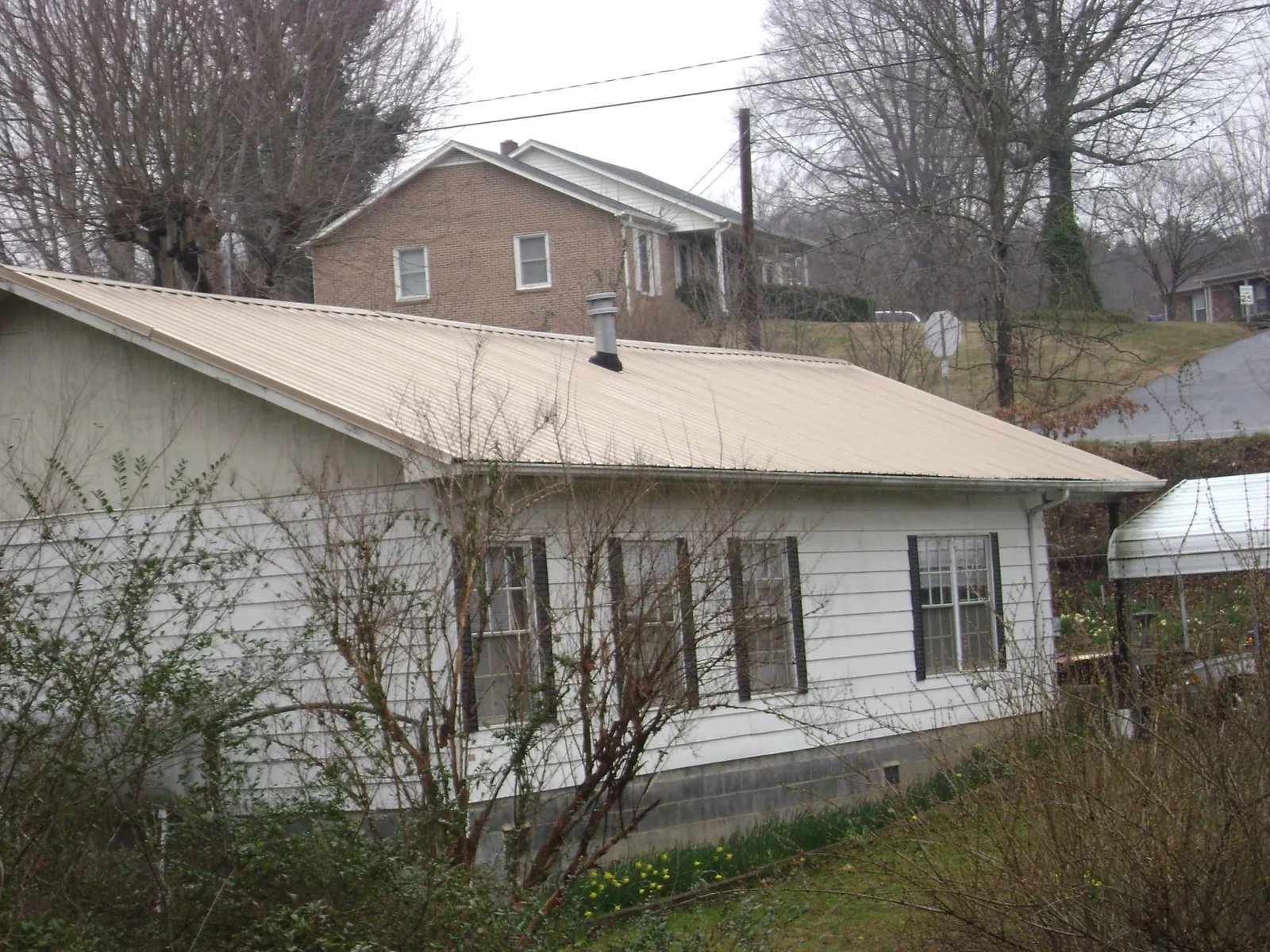 Tan metal roof on a white sided house set into a hillside — Commercial Roofing by Roofing Brothers in North Norwich