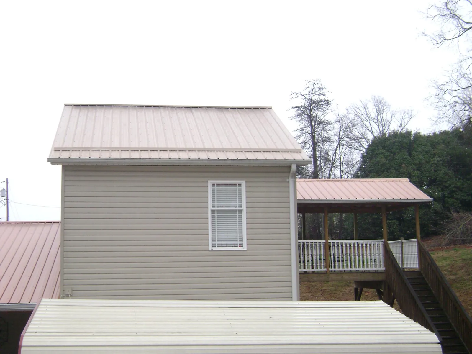 Tan metal roofs on a two story addition and attached porch, from a Roof Replacement job in North Norwich